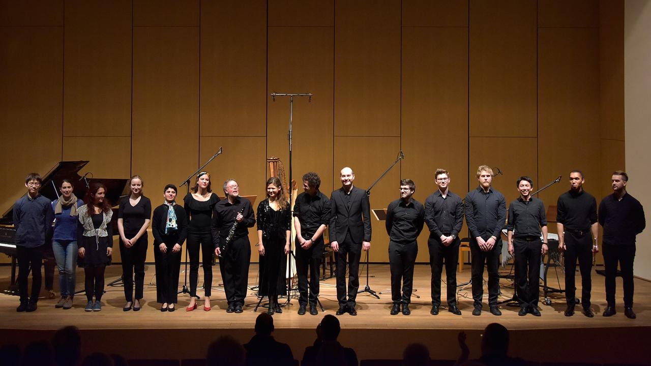 Das Ensemble 20/21 steht mit Dirigent David Smeyers in einer Reihe auf der Bühne Das Ensemble 20/21 steht mit Dirigent David Smeyers in einer Reihe auf der Bühne