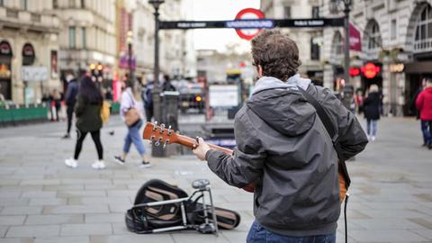 Ein Mann steht an einer U-Bahnstation in London und spielt Gitarre.