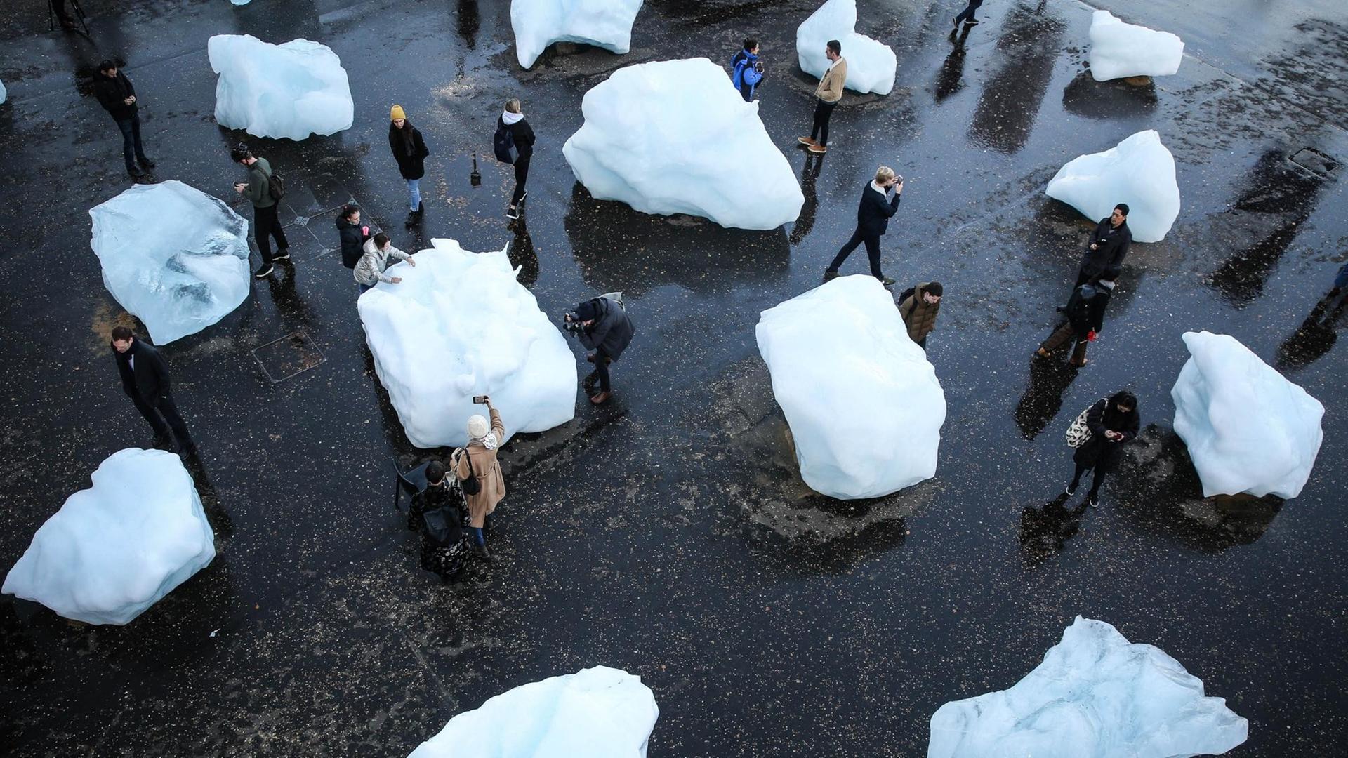 Auf einem Platz liegen große Eisblöcke. Zwischen den Eisblöcken laufen Menschen herum. Auf einem Platz liegen große Eisblöcke. Zwischen den Eisblöcken laufen Menschen herum.