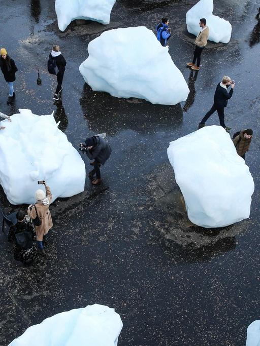 Auf einem Platz liegen große Eisblöcke. Zwischen den Eisblöcken laufen Menschen herum.