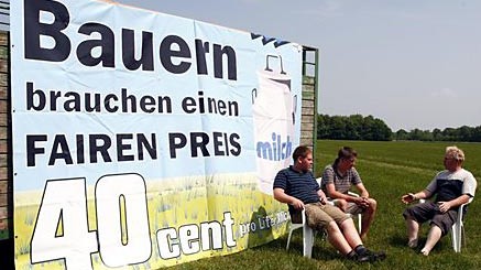 Bauern sitzen in Wiefelstede, Niedersachsen, neben der Zufahrt zur Molkerei Ammerland vor einem Protestplakat.