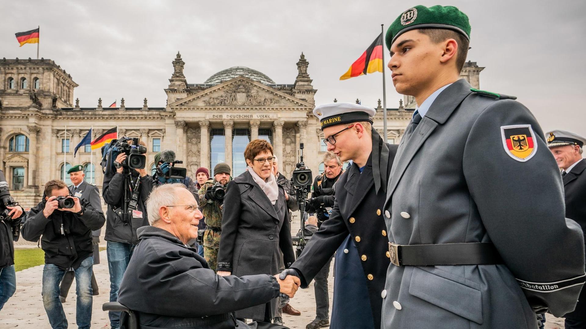 Wolfgang Schäuble gibt einem Rekruten der Marine die Hand, dahinter Verteidigungsministerin Kramp-Karrenbauer und Fotografen vor dem Reichstagsgebäude.