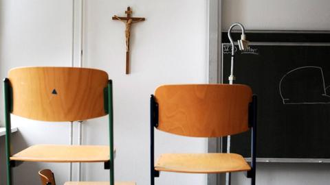 Hochgestellte Stühle in einem Klassenzimmer im Canisius-Kolleg - im Hintergrund an der Wand ein Kruzifix.