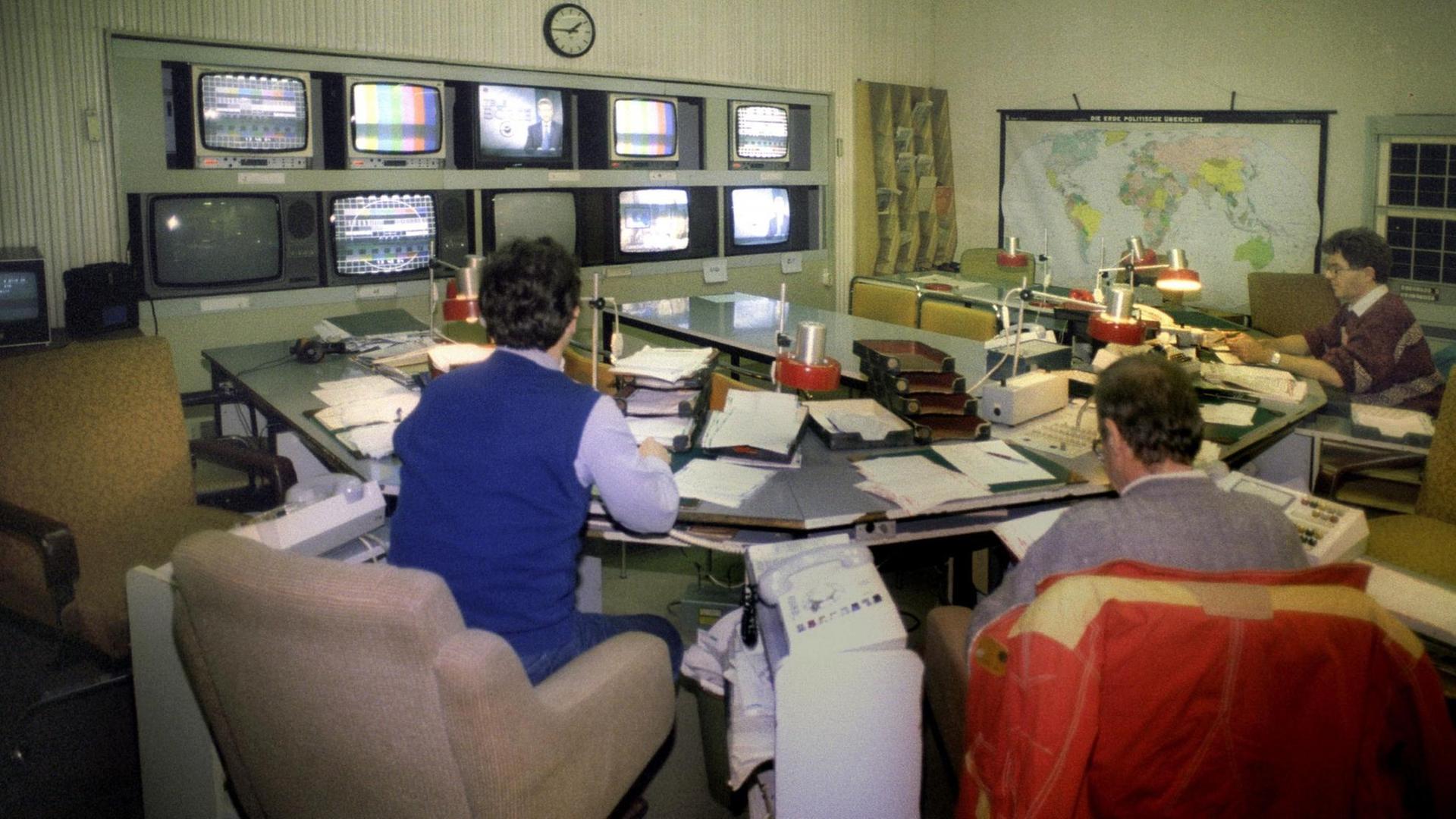 Nachrichtenraum der "Aktuelle Kamera" am 01.01.1991 in Adlershof. In einem Raum sitzen mehrere Männer, an der Wand befinden sich Monitore, neben Sesseln stehen Telefone. Nachrichtenraum der "Aktuelle Kamera" am 01.01.1991 in Adlershof. In einem Raum sitzen mehrere Männer, an der Wand befinden sich Monitore, neben Sesseln stehen Telefone.