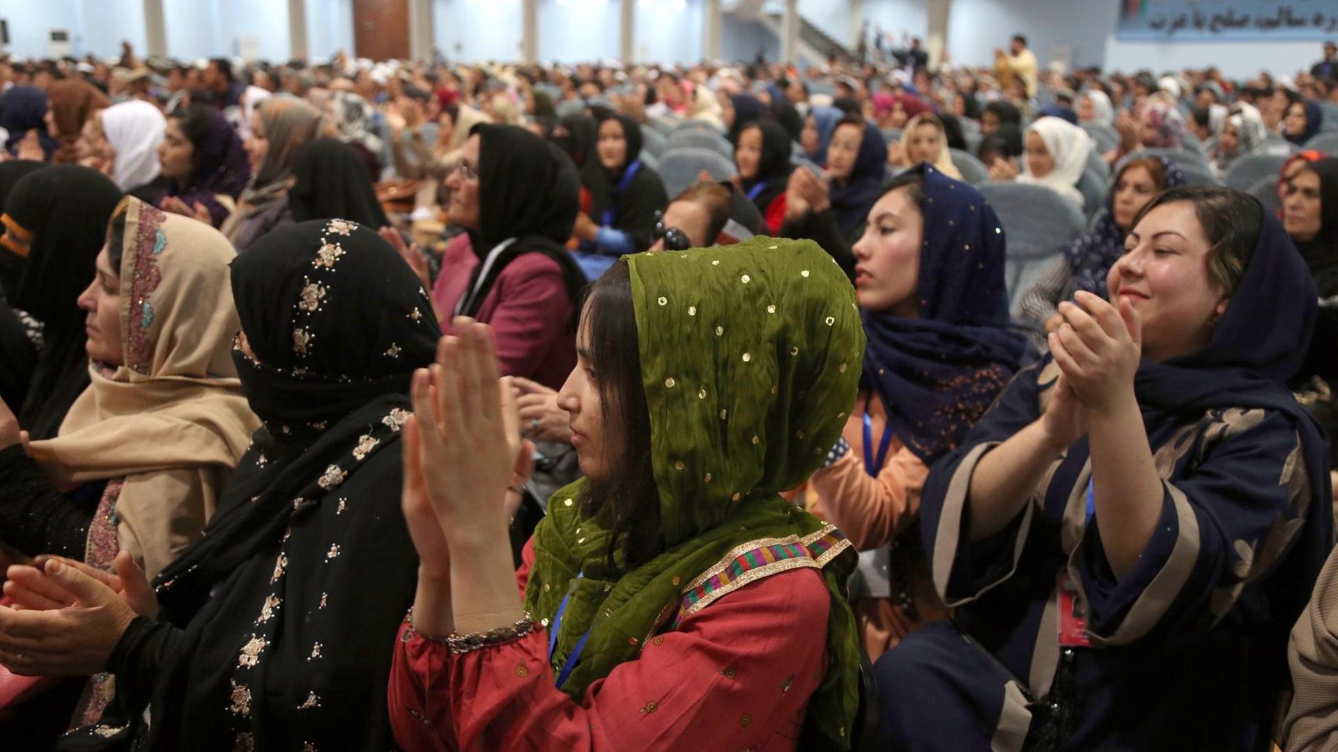 Frauen mit Kopftuch sitzen in einem großen Raumund klatschen. Frauen mit Kopftuch sitzen in einem großen Raumund klatschen.