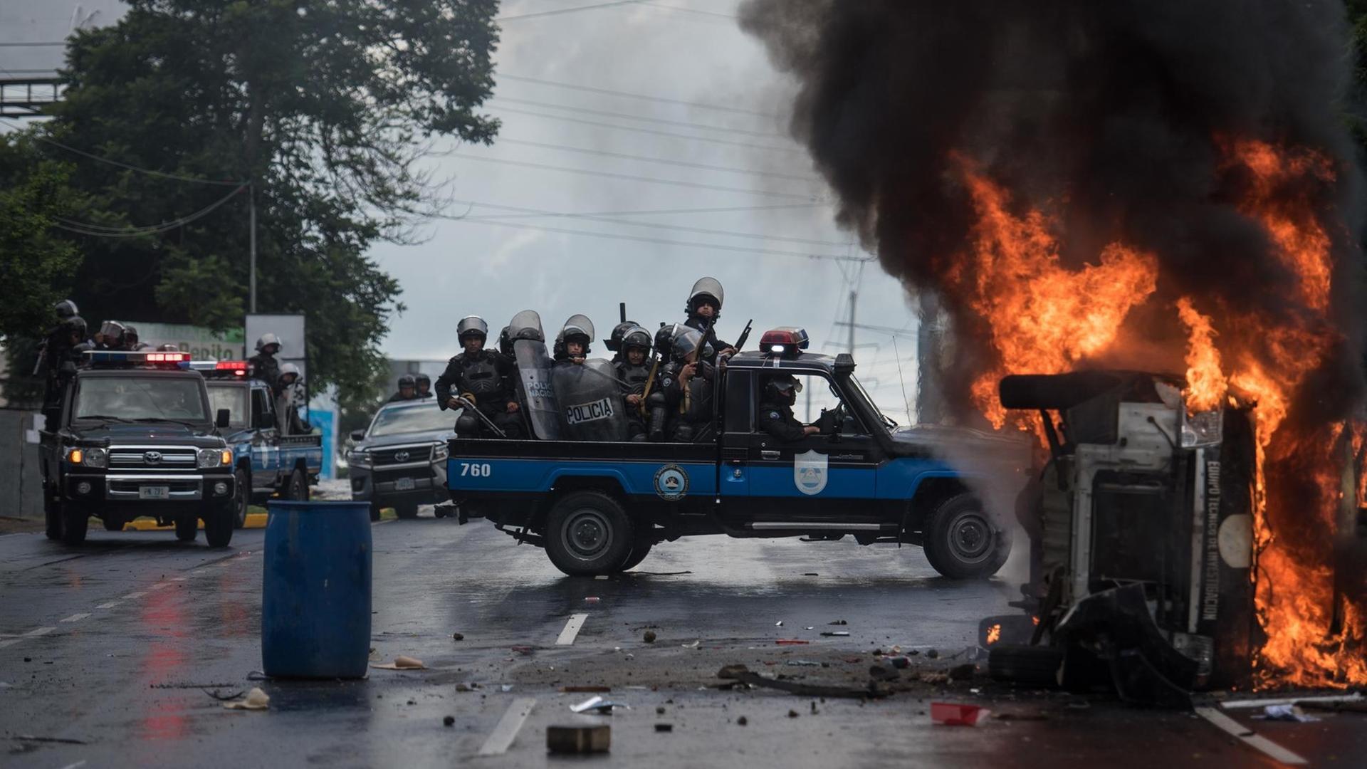 02.09.2018, Nicaragua, Managua: Schwer bewaffnete Polizisten sitzen auf einem Pick-up und stehen neben einem brennenden Polizeifahrzeug. Mindestens eine Person wurde in Managua verletzt als Unbekannte mit Schusswaffen auf die Teilnehmer einer Demonstration gegen die Regierung schossen. Foto: Carlos Herrera/dpa | Verwendung weltweit 02.09.2018, Nicaragua, Managua: Schwer bewaffnete Polizisten sitzen auf einem Pick-up und stehen neben einem brennenden Polizeifahrzeug. Mindestens eine Person wurde in Managua verletzt als Unbekannte mit Schusswaffen auf die Teilnehmer einer Demonstration gegen die Regierung schossen. Foto: Carlos Herrera/dpa | Verwendung weltweit