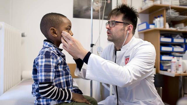 Arzt Hanno Klemm von der Malteser Migranten Medizin behandelt einen Jungen aus Guinea Aequatorial in der Praxis des Malteser Hilfsdienst in Berlin.