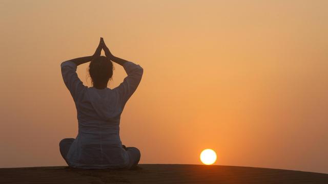 Eine Frau meditiert vor einem Sonnenuntergang.