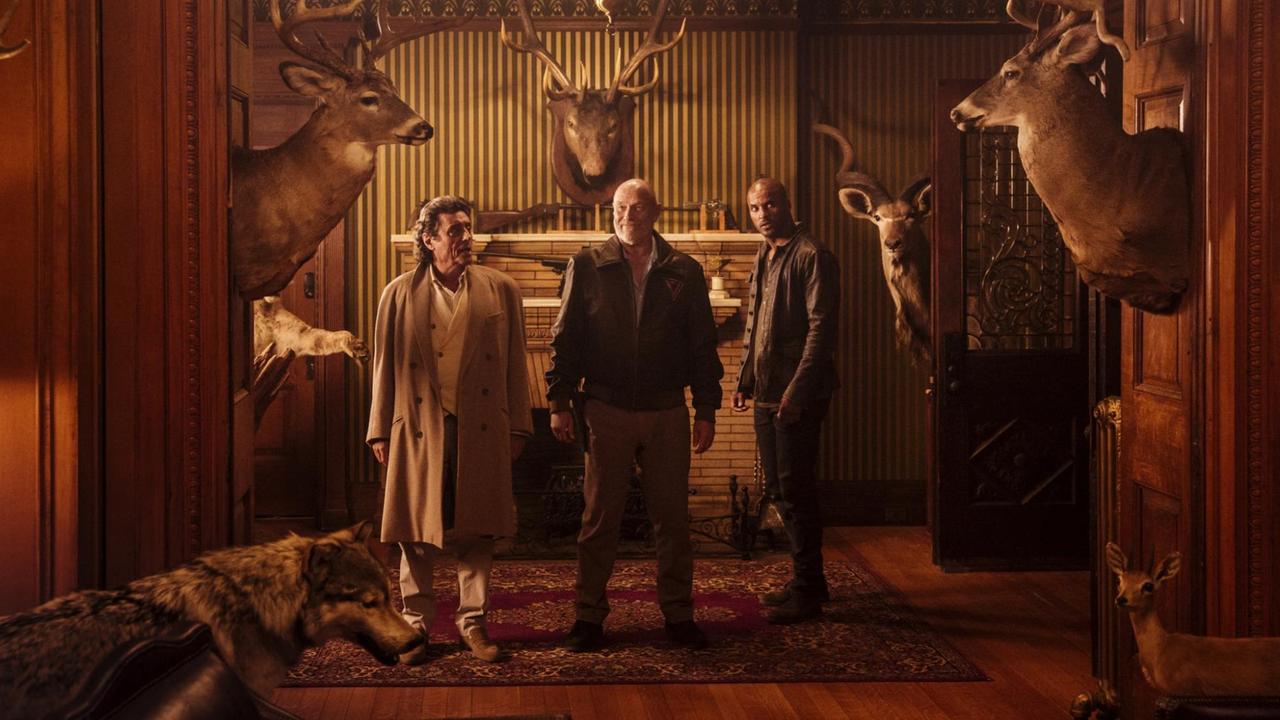 Mr Wednesday (Ian McShane, links) und Shadow Moon (Ricky Whittle, rechts) stehen mit dem Gott Vulcan (Corbin Bernsen) in einem Raum mit Hirschgeweihen und ausgestopften Tieren