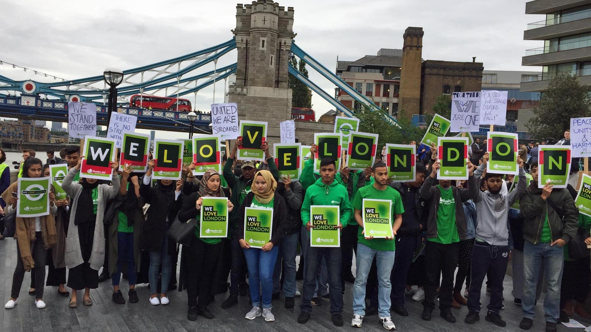 Menschen stehen vor der London Bridge und halten Schilder mit "We love London" in die Höhe.
