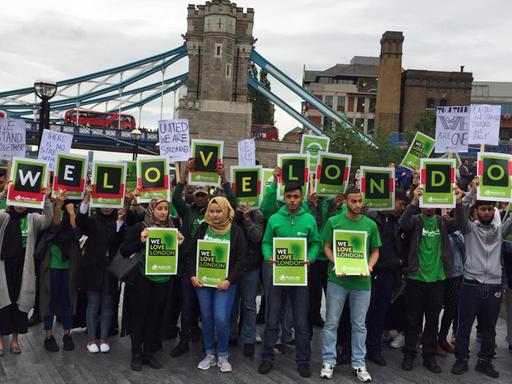 Menschen stehen vor der London Bridge und halten Schilder mit "We love London" in die Höhe.