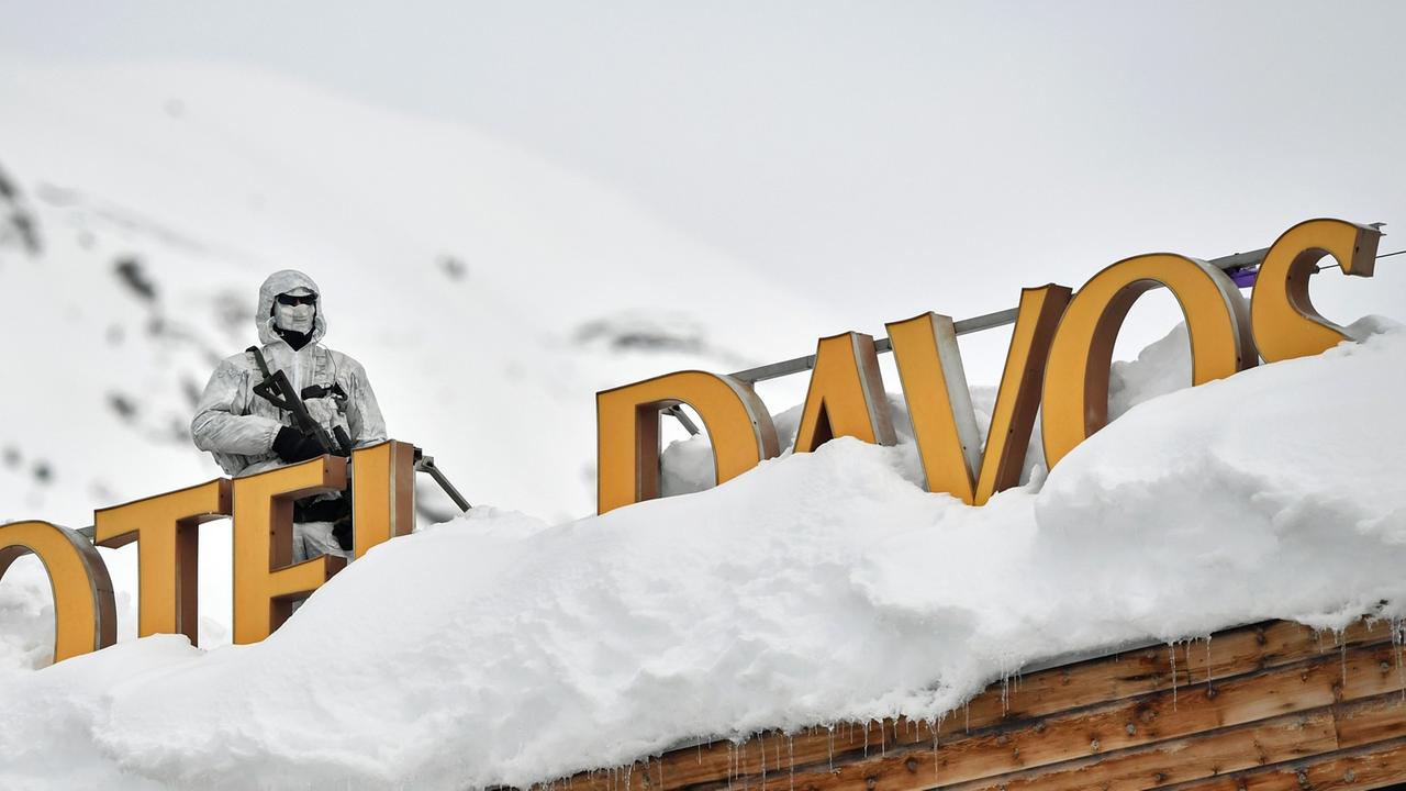 Ein Polizist in Tarnkleidung steht mit einem Maschinengewehr auf einem Dach mit der Schrift "Hotel Davos".