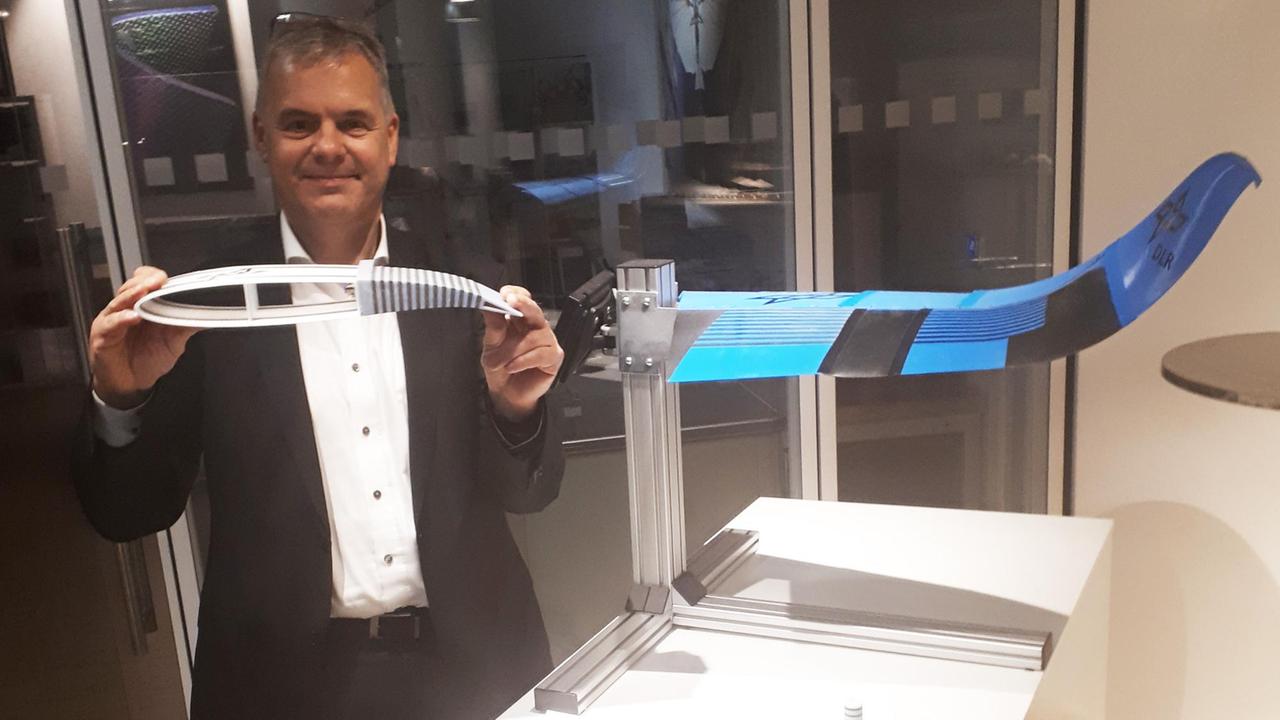 Martin Wiedemann, Leiter des Braunschweiger Instituts für Faserverbundleichtbau und Adaptronik des Deutschen Zentrums für Luft- und Raumfahrt. Ein Mann steht in einem Raum und hält ein kleines Modell einer Tragfläche in der Hand.