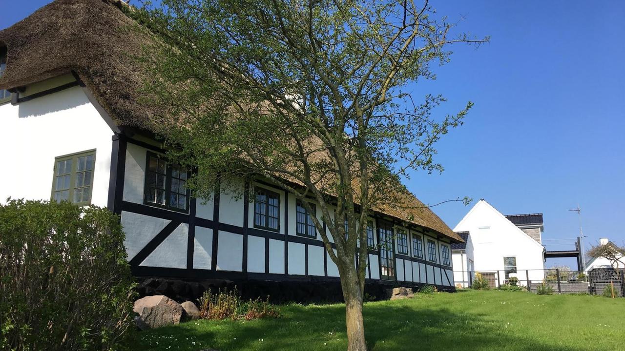 Ein langgezogeses weißes Fachwerkhaus, umringt von Wiese und Bäumen. Ein langgezogeses weißes Fachwerkhaus, umringt von Wiese und Bäumen.