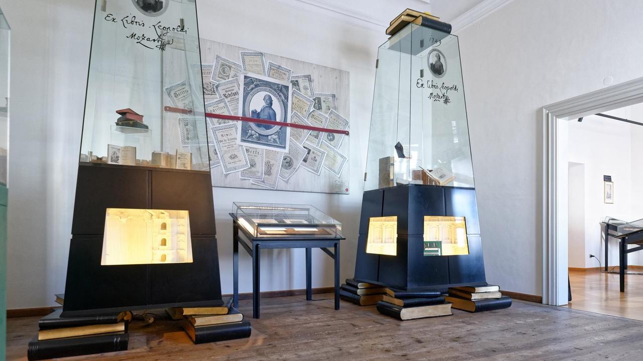 Das Bild zeigt Glasvitrinen mit Büchern und ein Bild, auf dem Leopold Mozart und einige Urkunden abgebildet sind Das Bild zeigt Glasvitrinen mit Büchern und ein Bild, auf dem Leopold Mozart und einige Urkunden abgebildet sind