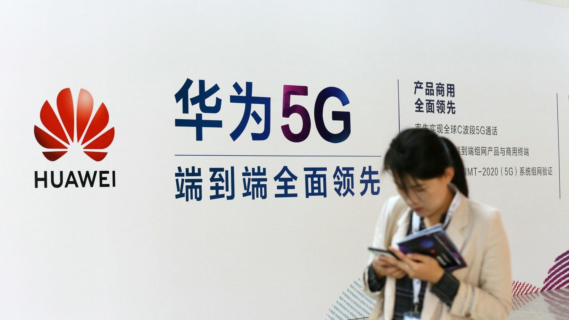 Eine Frau geht an einem Stand des chinesischen Technologiekonzerns Huawei mit Werbung für die 5G-Technik auf der Messe PT in Peking vorbei Eine Frau geht an einem Stand des chinesischen Technologiekonzerns Huawei mit Werbung für die 5G-Technik auf der Messe PT in Peking vorbei