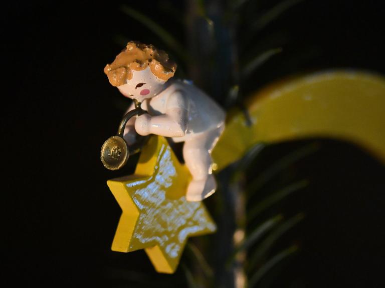 Anhänger an einem Weihnachtsbaum: Ein Holzengel, der in ein Horn bläst, sitzt auf einem Stern mit Schweif.