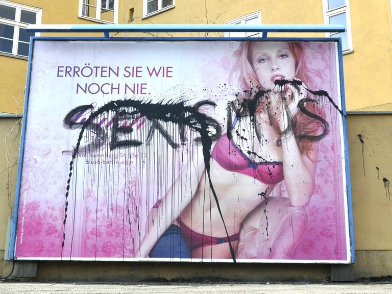 Über ein Plakat, dasss eine Frau in Dessous zeigt steht mit schwarzer Sprühfarbe "Sexismus" geschrieben.
