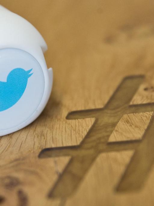Ein Gadget mit dem Logo des Kurznachrichtendienstes Twitter Deutschland auf einem Besprechungstisch mit eingraviertem Zeichen Hashtag.