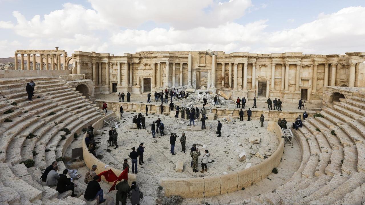 Sie sehen ein theaterähnliches Bauwerk in Palmyra und Journalisten, die sich Anfang März 2017 ein Bild von der Lage in der Stadt machen.