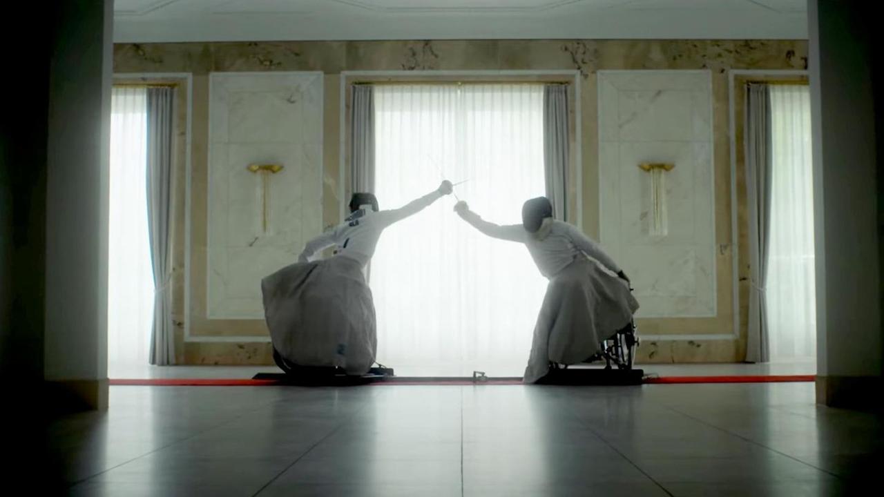 Filmstill aus der Kampagne "Choose hard. Never easy" vom Team Deutschland Paralympics. Zu sehen sind zwei fechtende Personen im Rollstuhl auf der Planche in einem historischen Saal. Filmstill aus der Kampagne "Choose hard. Never easy" vom Team Deutschland Paralympics. Zu sehen sind zwei fechtende Personen im Rollstuhl auf der Planche in einem historischen Saal.