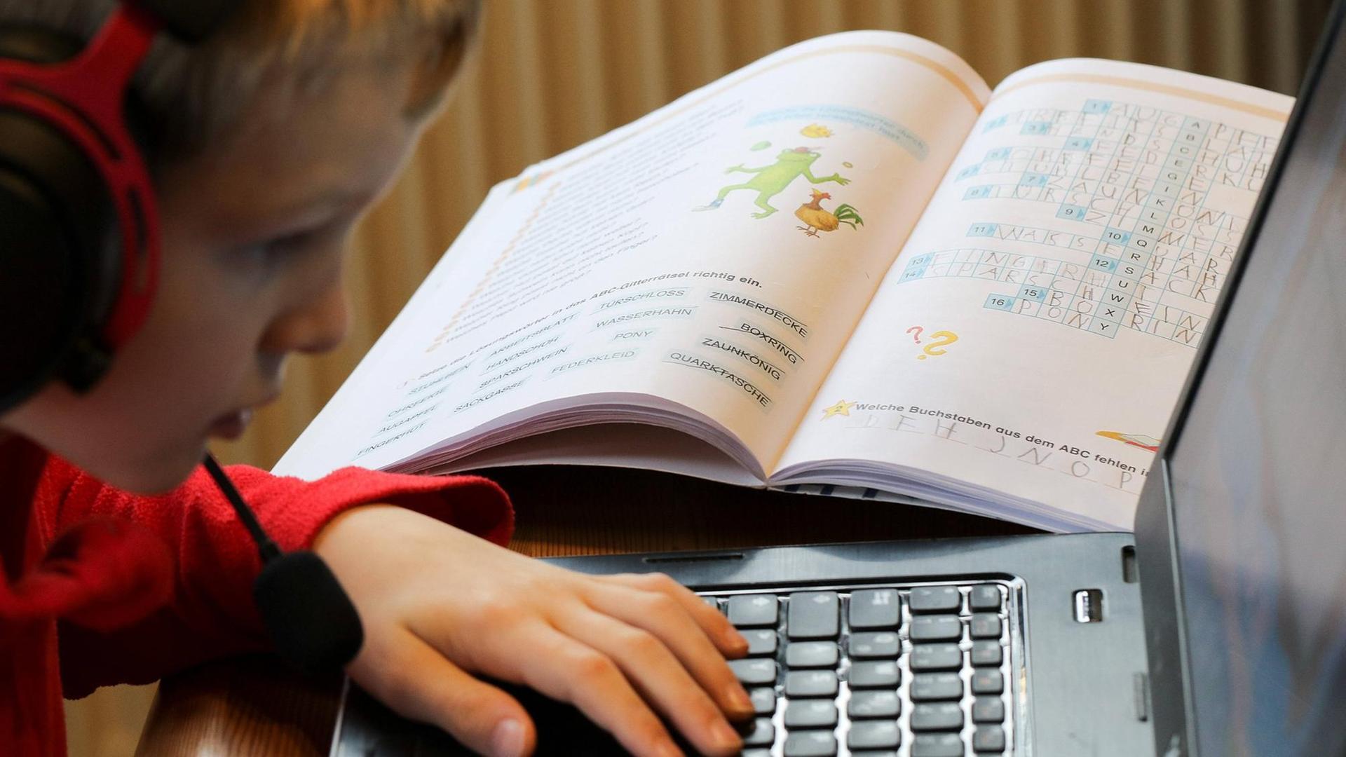 Eine Junge sitzt vor einem aufgeklappten Laptop mit Kopfhörern und Mikrofon und macht Homeschooling. Auf dem Tisch liegen verschiedene Schulbücher. Eine Junge sitzt vor einem aufgeklappten Laptop mit Kopfhörern und Mikrofon und macht Homeschooling. Auf dem Tisch liegen verschiedene Schulbücher.