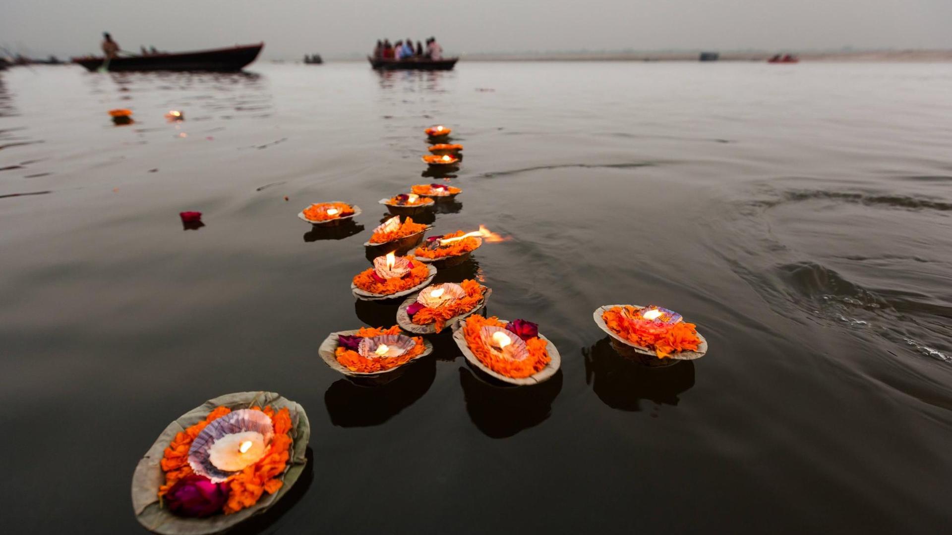 Mehrere auf Blättern orangenen Blüten gesetzte Kerzen schwimmen auf dem Wasser. Mehrere auf Blättern orangenen Blüten gesetzte Kerzen schwimmen auf dem Wasser.