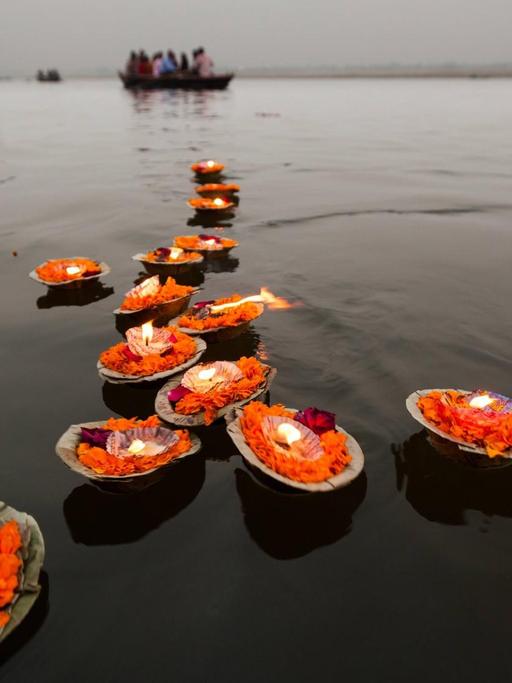Mehrere auf Blättern orangenen Blüten gesetzte Kerzen schwimmen auf dem Wasser.