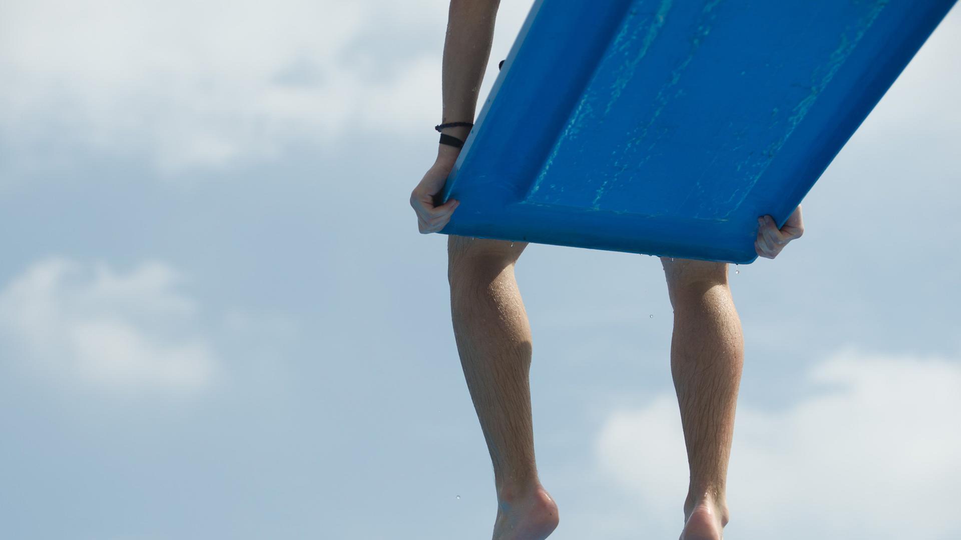 Ein Junge sitzt auf einem Sprungbrett im Freibad und lässt die Beine baumeln, sichtbar sind nur die Beine. Ein Junge sitzt auf einem Sprungbrett im Freibad und lässt die Beine baumeln, sichtbar sind nur die Beine.