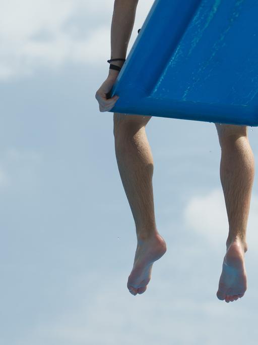 Ein Junge sitzt auf einem Sprungbrett im Freibad und lässt die Beine baumeln, sichtbar sind nur die Beine.