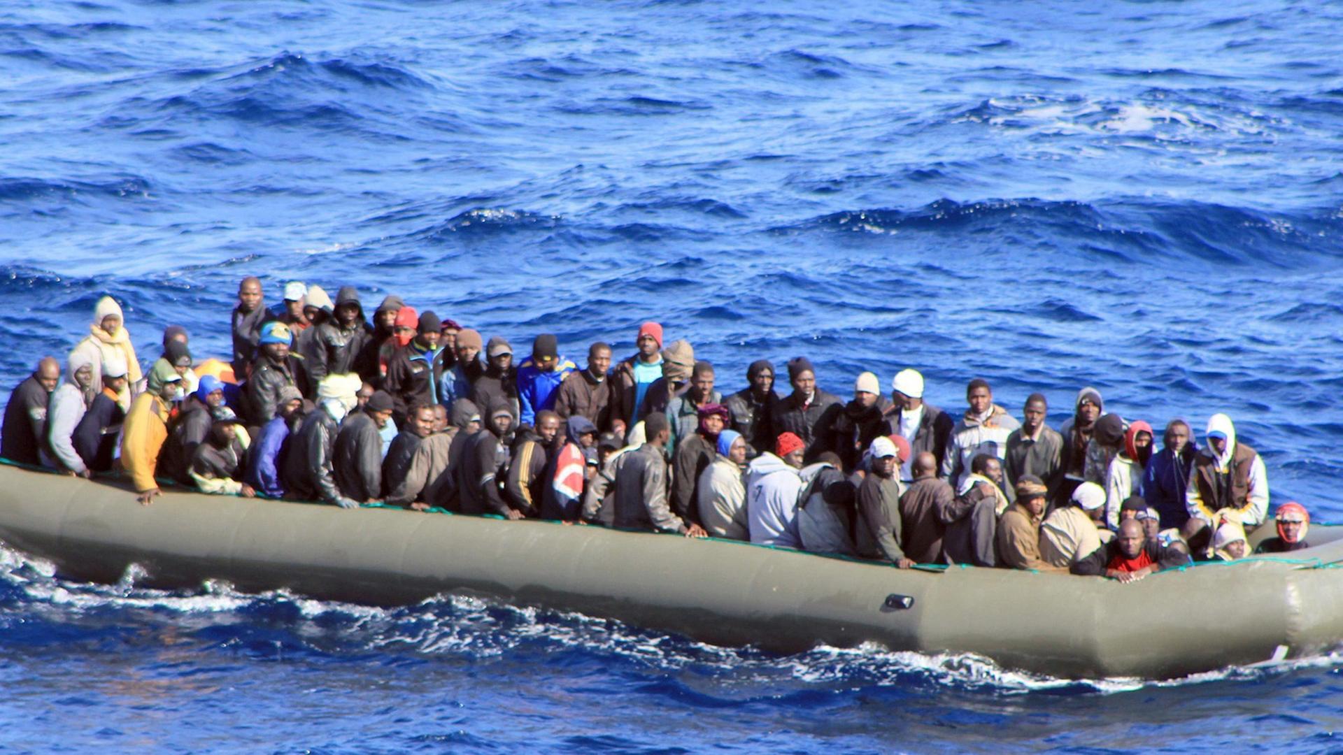 Ein überfülltes großes Schlauchboot mit mehreren Dutzend Menschen treibt auf dem Wasser. Ein überfülltes großes Schlauchboot mit mehreren Dutzend Menschen treibt auf dem Wasser.