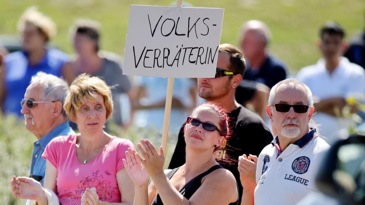 Eine Frau steht mit einem Schild "Volksverräterin" am 26.08.2015 vor einer Flüchtlingsunterkunft in Heidenau (Sachsen) und wartet auf Bundeskanzlerin Merkel. Die Kanzlerin besucht die Flüchtlingsunterkunft.