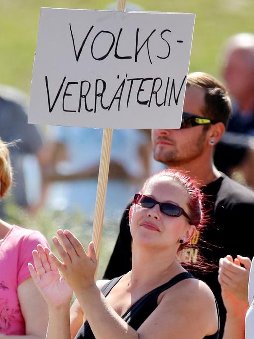 Eine Frau steht mit einem Schild "Volksverräterin" am 26.08.2015 vor einer Flüchtlingsunterkunft in Heidenau (Sachsen) und wartet auf Bundeskanzlerin Merkel. Die Kanzlerin besucht die Flüchtlingsunterkunft.