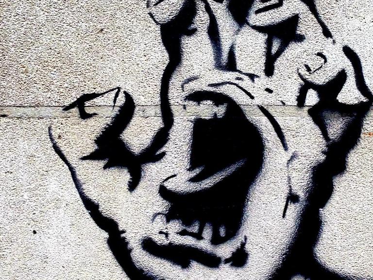 Ein Grafitti zeigt eine Handfläche, in deren Mitte ein Mund aufgerissen schreit.