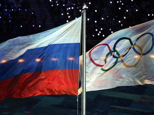 Die Olympische Flagge (r) und die russische Flagge flattern am 23.02.2014 während der Abschlussfeier bei den Olympischen Spielen 2014 in Sotschi, Russland.