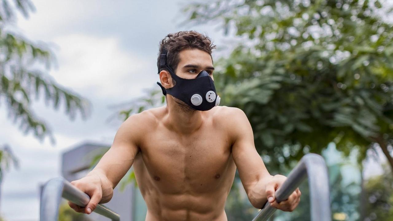 Ein Sportler, der mit einer schwarzen Atemmaske an einem Barren in freiem Oberkörper trainiert. Ein Sportler, der mit einer schwarzen Atemmaske an einem Barren in freiem Oberkörper trainiert.