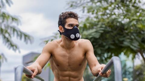 Ein Sportler, der mit einer schwarzen Atemmaske an einem Barren in freiem Oberkörper trainiert.