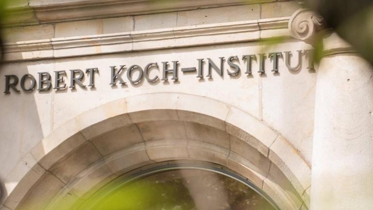 Der Eingang des Robert Koch-Instituts ist mit seinem Namenslogo durch Bäume hindurch zu sehen. Der Eingang des Robert Koch-Instituts ist mit seinem Namenslogo durch Bäume hindurch zu sehen.