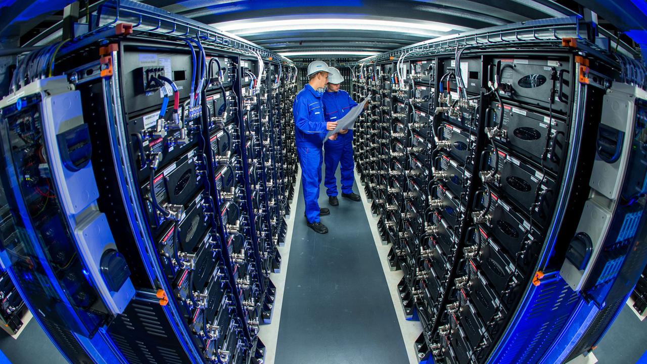 Zwei Auszubildende stehen zwischen Stromspeichern im größten kommerziellen Batteriespeicher Europas. Zwei Auszubildende stehen zwischen Stromspeichern im größten kommerziellen Batteriespeicher Europas.