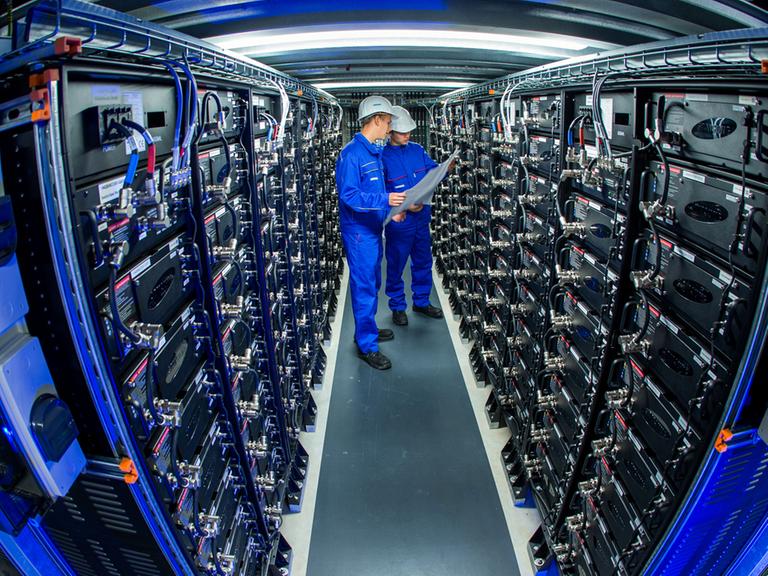 Zwei Auszubildende stehen zwischen Stromspeichern im größten kommerziellen Batteriespeicher Europas.