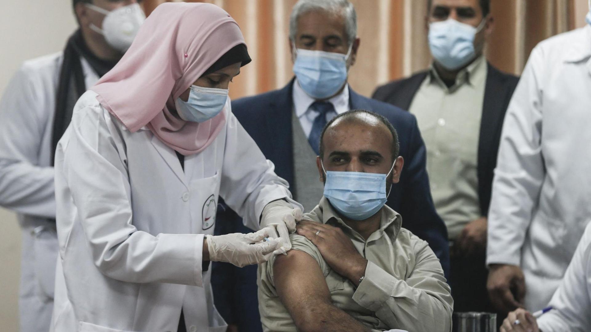 Ein Palästinenser bekommt eine Corona-Impfung von einer Krankenschwester. Um ihn herum stehen noch vier Personen.