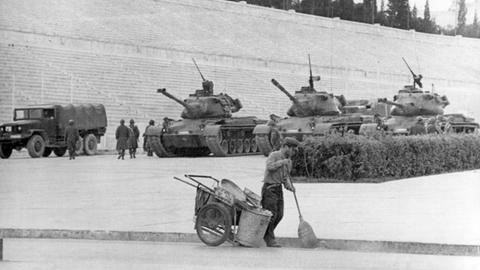 Unbeeindruckt von den Panzern geht im April 1967 ein Straßenkehrer im Stadion von Athen seiner Arbeit nach.