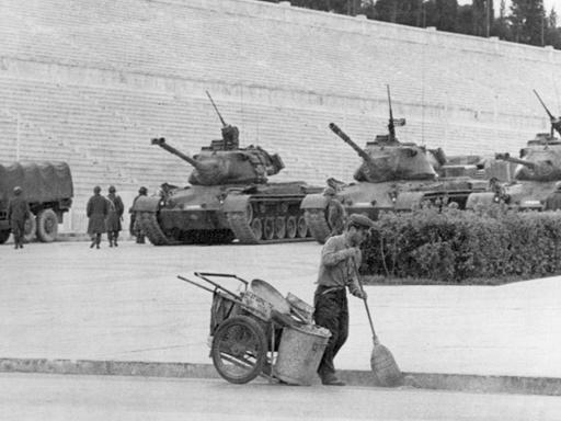 Unbeeindruckt von den Panzern geht im April 1967 ein Straßenkehrer im Stadion von Athen seiner Arbeit nach.