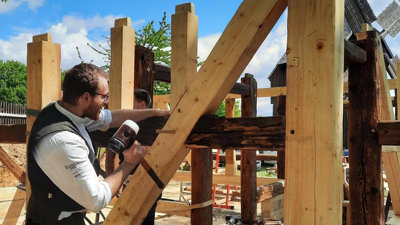 Ein Zimmerermeister arbeitet an den Balken eines Fachwerkhauses, das wieder aufgebaut werden soll. Ein Zimmerermeister arbeitet an den Balken eines Fachwerkhauses, das wieder aufgebaut werden soll.