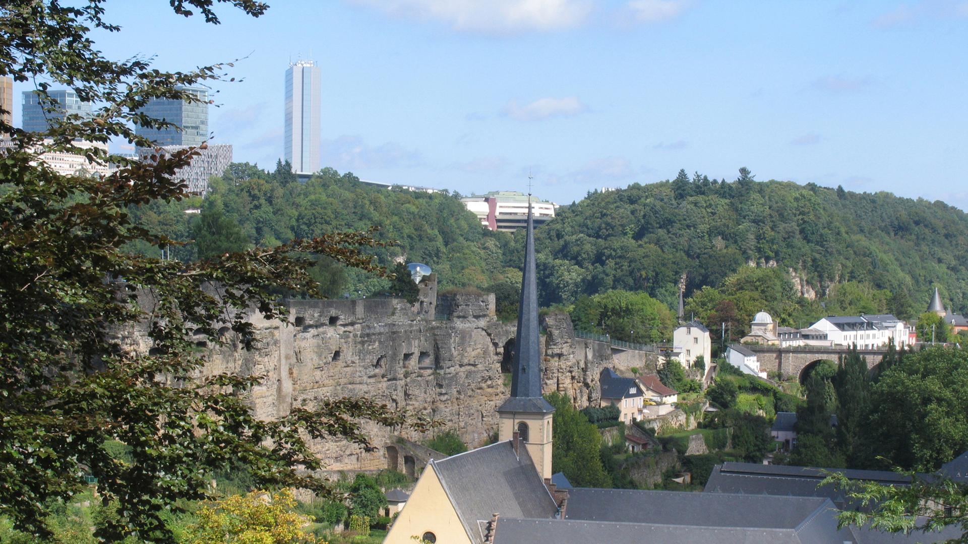 Die Burg Lucilinburhuc befindet sich in einer Höhe von rund 282 m auf dem so genannten Bockfelsen, den Graf Siegfried 963 erwarb. Darunter die Teilansicht der Kasematten. Im Hintergrund der Kirchberg mit seiner Skyline. Die Burg wird in einer Urkunde erwähnt, welche den Tausch zwischen dem Ardennergraf Siegfried und dem Kloster St. Maximin in Trier aus dem Jahre 963 dokumentiert. Aus dem Besitz des Klosters erhält der Graf den Bockfelsen gegen Ländereien in Feulen. Die Burg Lucilinburhuc befindet sich in einer Höhe von rund 282 m auf dem so genannten Bockfelsen, den Graf Siegfried 963 erwarb. Darunter die Teilansicht der Kasematten. Im Hintergrund der Kirchberg mit seiner Skyline. Die Burg wird in einer Urkunde erwähnt, welche den Tausch zwischen dem Ardennergraf Siegfried und dem Kloster St. Maximin in Trier aus dem Jahre 963 dokumentiert. Aus dem Besitz des Klosters erhält der Graf den Bockfelsen gegen Ländereien in Feulen.