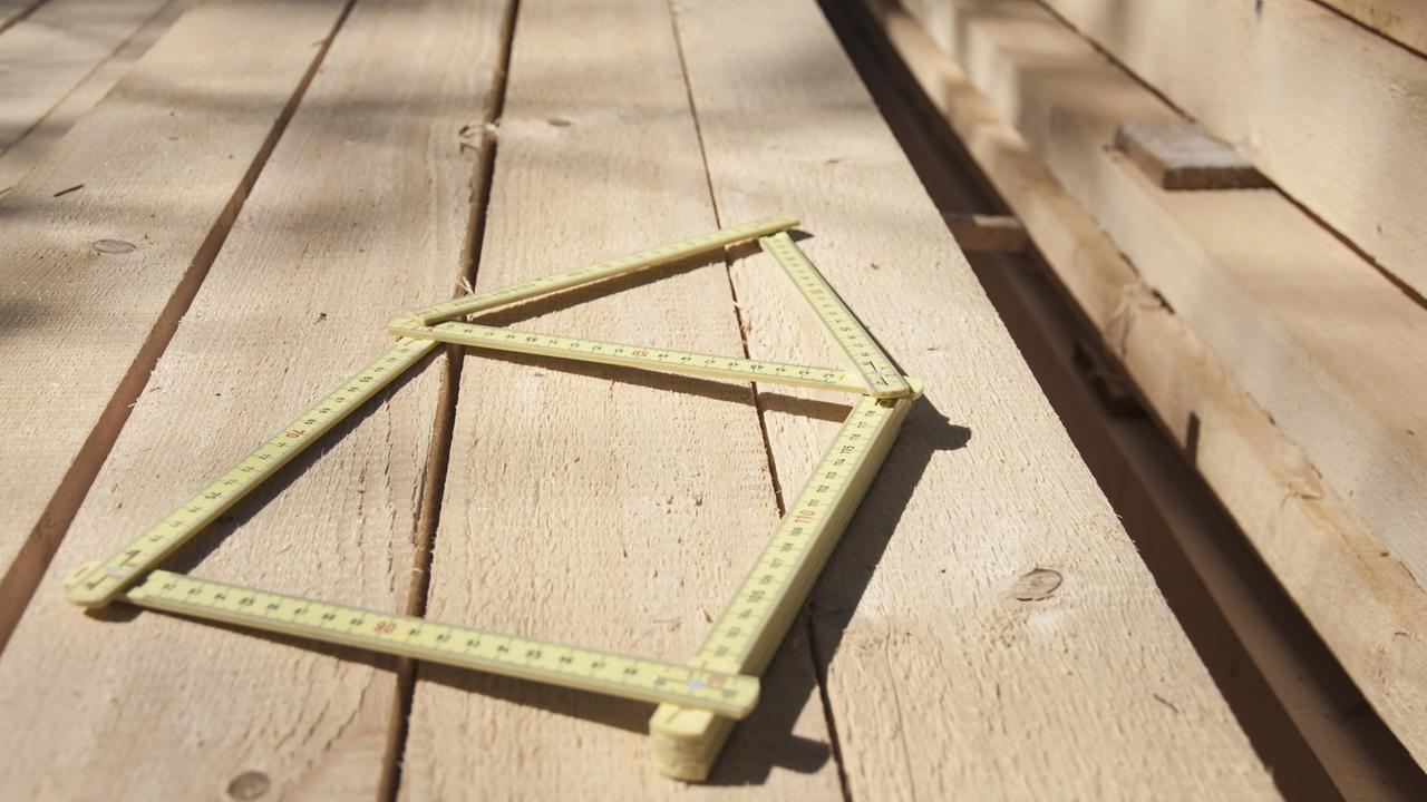 Ein zum Haus gefalteter Zollstock auf einem Holzfußboden. Ein zum Haus gefalteter Zollstock auf einem Holzfußboden.