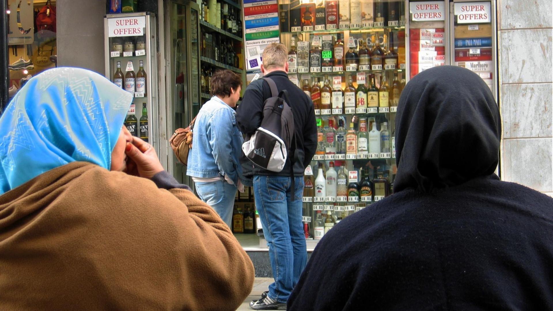 Zwei Musliminnen vor einem Laden mit Tabakwaren und alkoholischen Getränken Zwei Musliminnen vor einem Laden mit Tabakwaren und alkoholischen Getränken