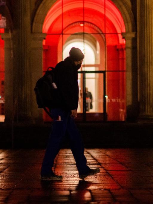 Ein Mann geht am frühen Morgen an der rot illuminierten Oper in Hannover vorbei.