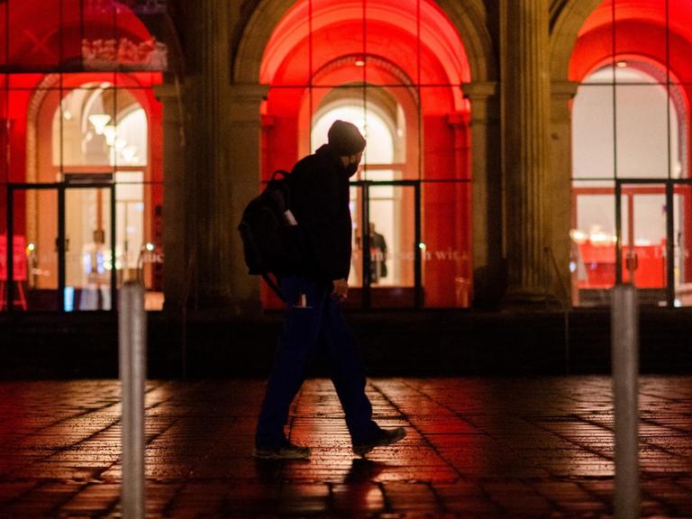 Ein Mann geht am frühen Morgen an der rot illuminierten Oper in Hannover vorbei.