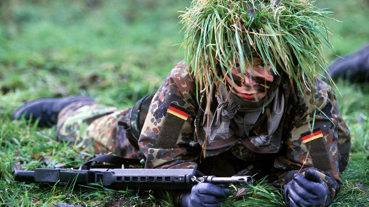 Eine Bundeswehrsoldatin robbt getarnt über eine Wiese. Eine Bundeswehrsoldatin robbt getarnt über eine Wiese.